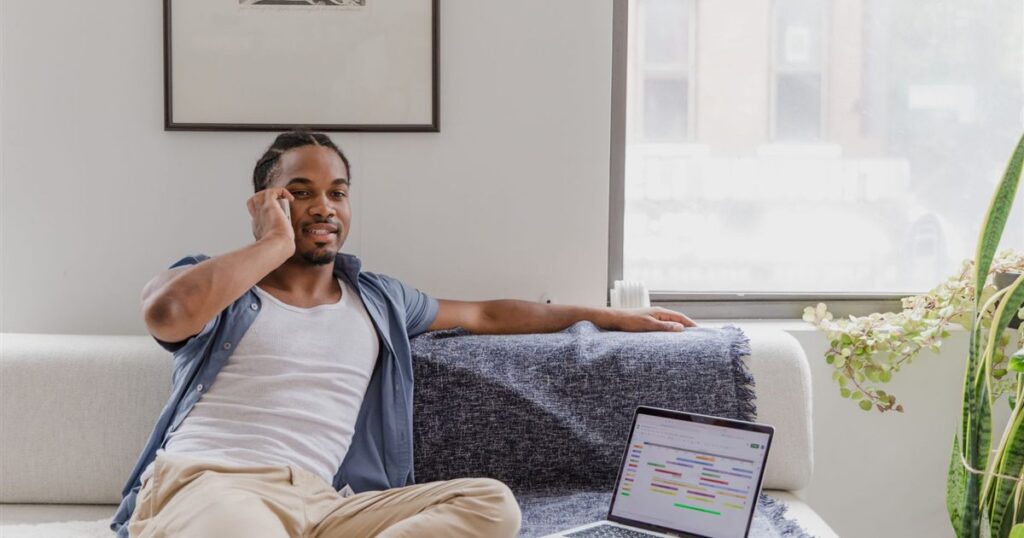 Man using his phone and laptop at home to borrow $100 online in Canada