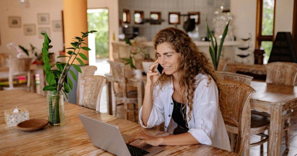 Smiling woman on her phone and laptop applying to borrow $500 online in Canada