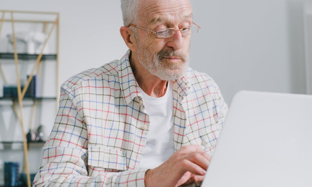 Senior man reviewing online loan FAQs in Canada on a laptop