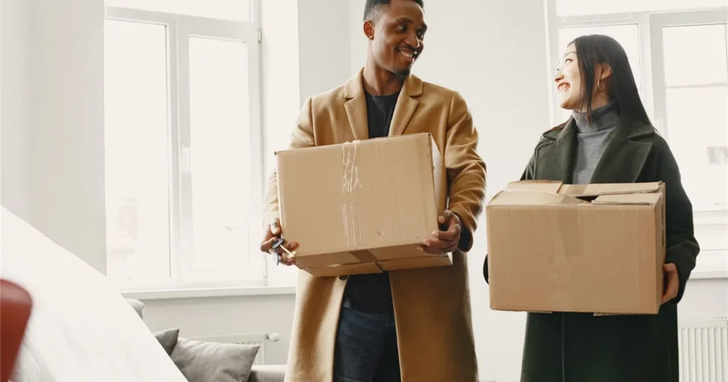Happy couple carrying boxes into a new home after they borrow money for moving in Canada