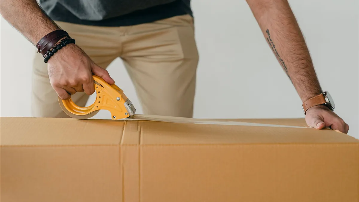 Man sealing a moving box with a tape gun while packing up a Canadian apartment