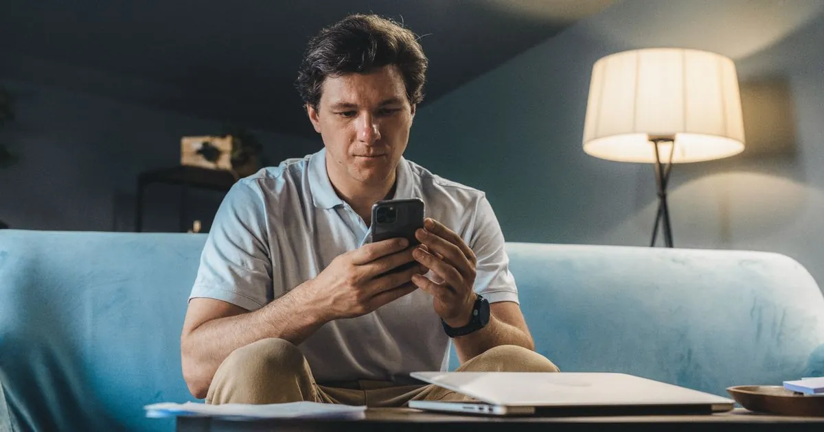 Man applying for quick payday loans online from his phone on the sofa in the evening