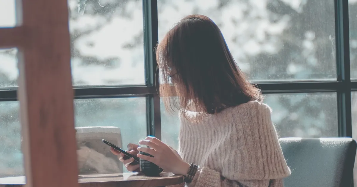Woman at a cafe window checking her phone for the realistic ways to get money now in Canada