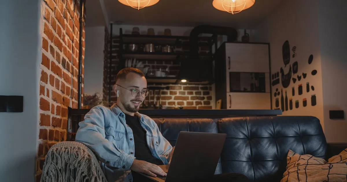 Man on a sofa at night comparing his options for money now on a laptop, with funding due the next morning