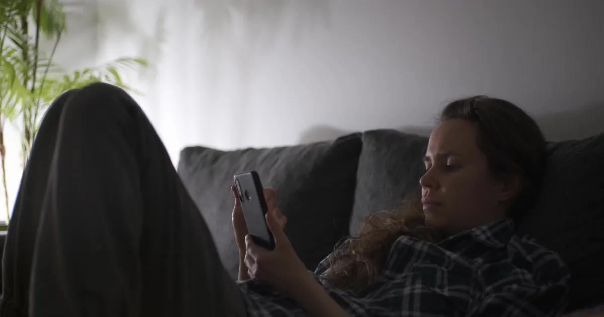 Woman on a sofa in the evening completing an application for online loans Alberta lenders fund the next morning